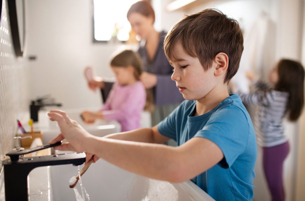 boy brushing his teeth with sisters and mother in bathroom