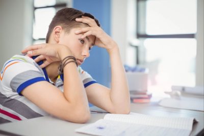 school-aged-boy-resting-head-on-hand-sitting-at-cl-2026-01-09-11-57-14-utc (1) Young boy sitting at a desk looking troubled